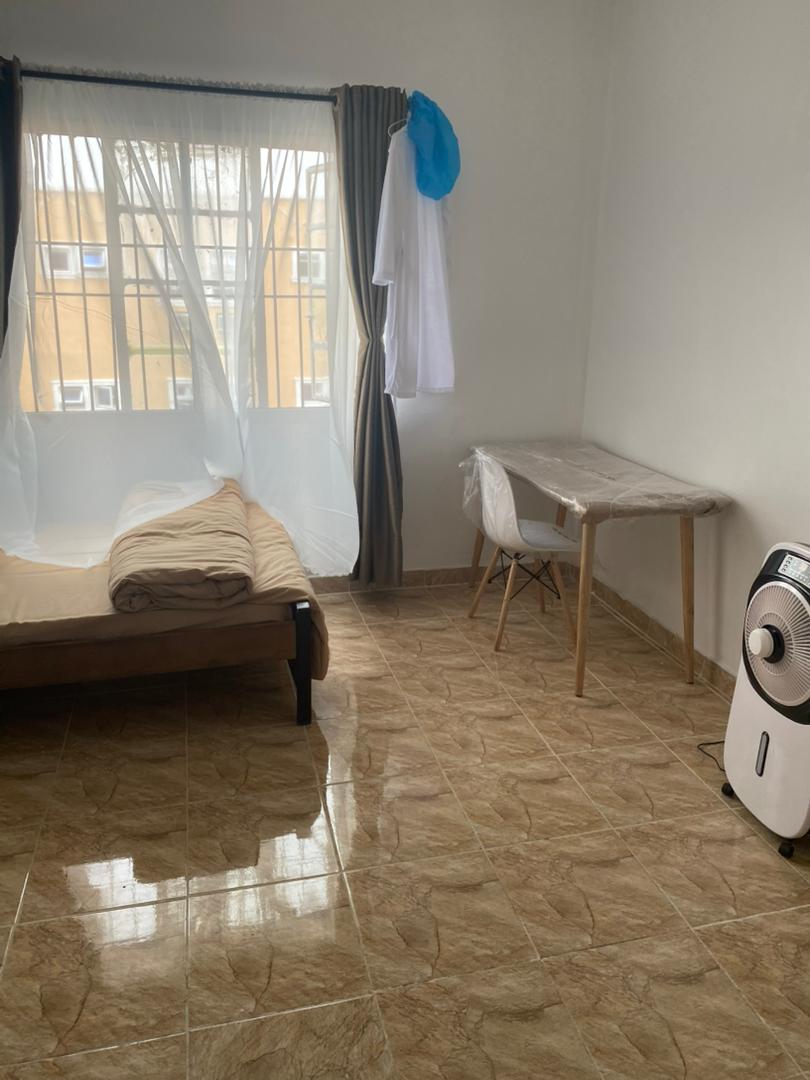 Bright single room with air cooler fan, sheer curtains, desk, and freshly made bed at Ajala Homes